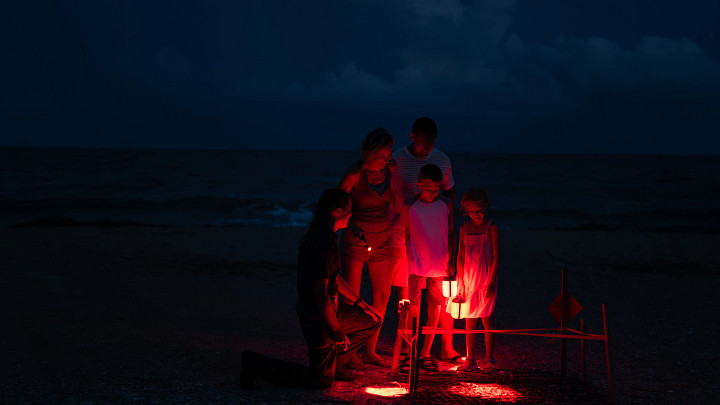 family on the beach at night with red light lamps